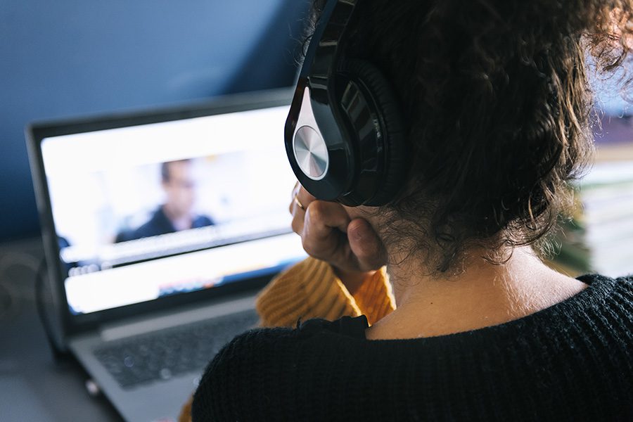 Video Library - Close Up Behind a Woman Wearing Headphones with Her Hair Up in a Bun and She is Watching a Video on a Laptop in Front of Her